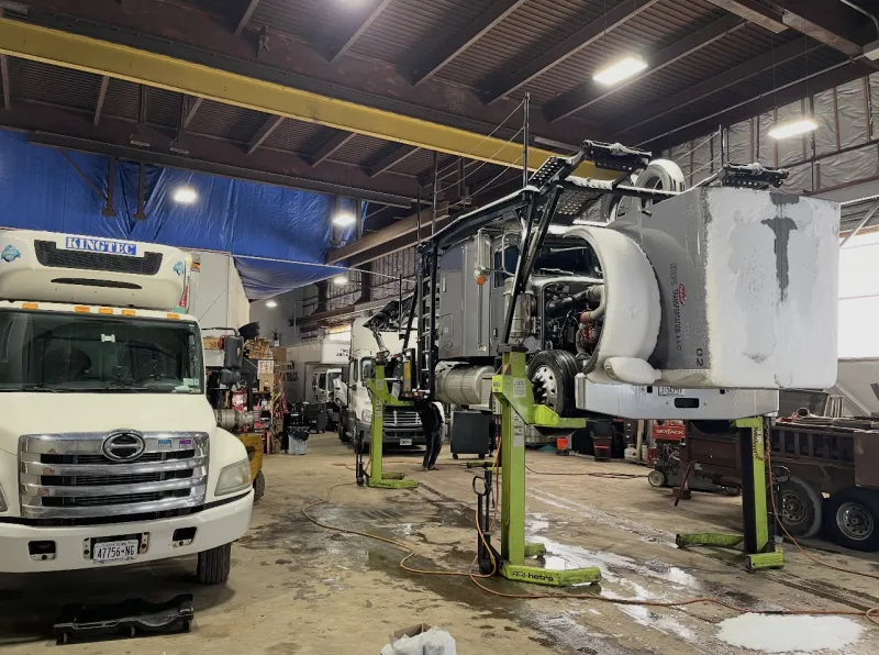 Semi raised on four green column lifts in the Top Guns bay, hood tilted forward.