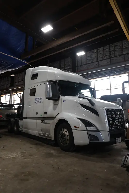 Front three-quarter of a white Volvo sleeper tractor inside the Top Guns bay.