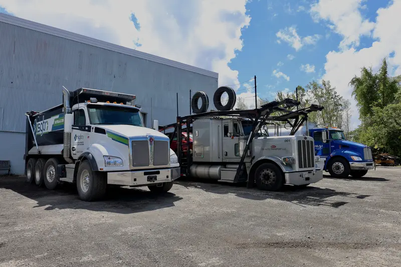 Kenworth dump truck, Peterbilt car hauler, and blue fuel truck parked in front of the shop.